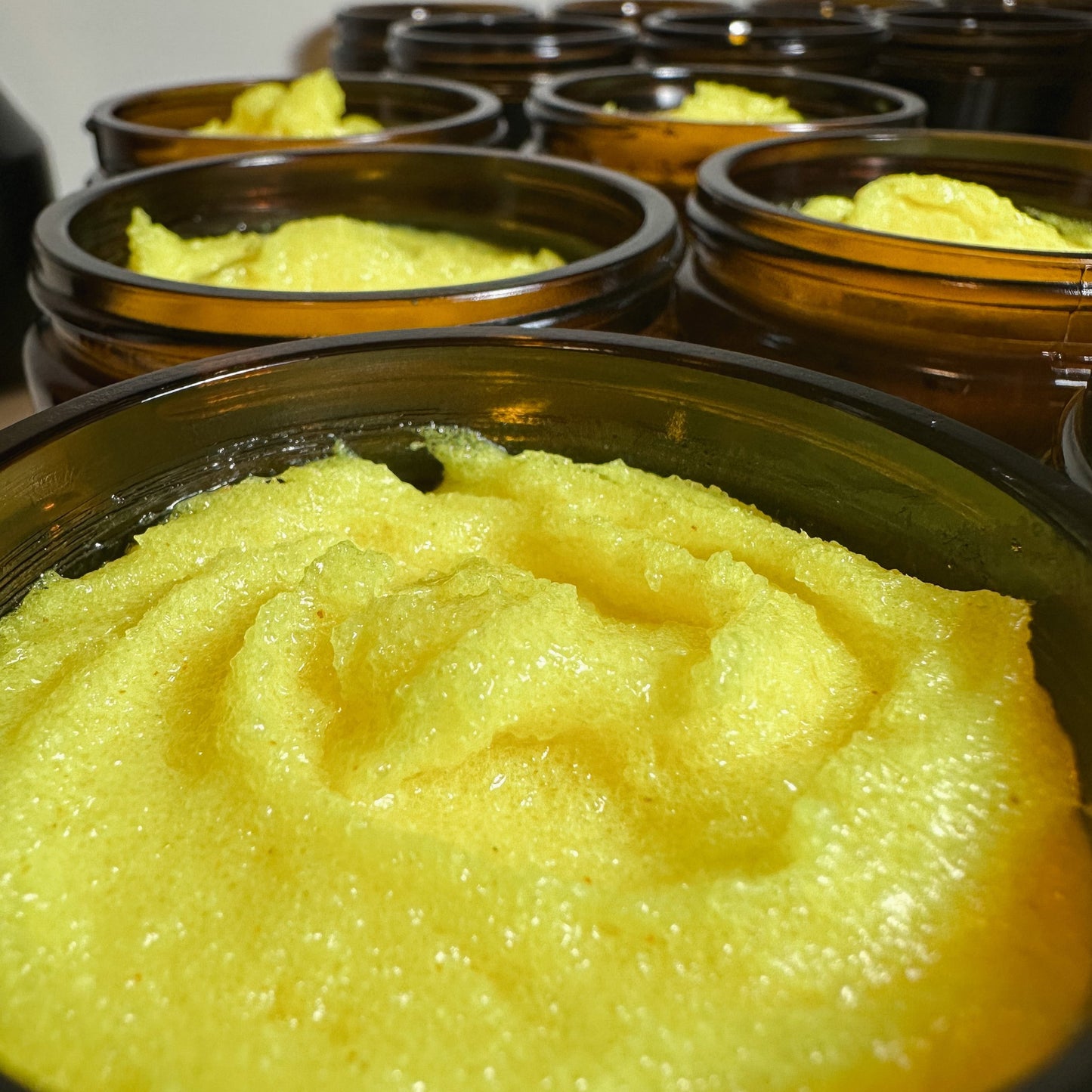 An open amber glass jar of Nuska Lemon & Turmeric Body Scrub, showing the scrub's texture.